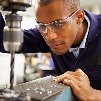 Worker using drill press wearing glasses